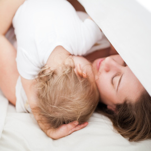 Mother embraces baby girl on bed under white sheet