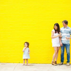 Mother and father eat ice cream with daughter next to yellow wall
