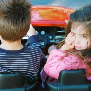 Girl rubs eyes next to brother in toy car