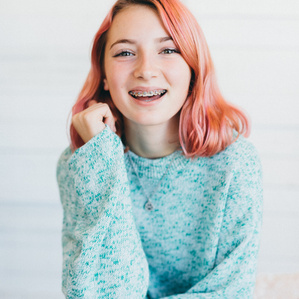 Teenage girl with braces and pink hair smiles at camera