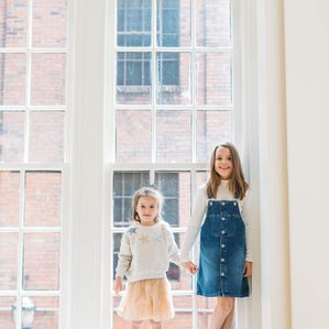 Two sisters stand in big window sill together