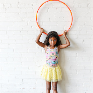 Girl holds hula hoop above her head by white wall