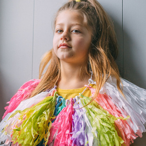 Young girl poses on wall with rainbow tassel necklace