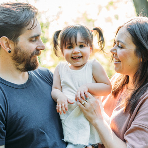Mother and father hold baby between them smiling in golden hour sunset light