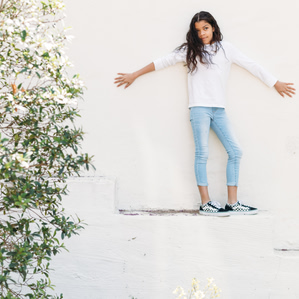 Girl stands on white wall next to garden