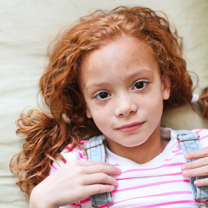 Beautiful red head girl with freckles and overalls lays on couch 