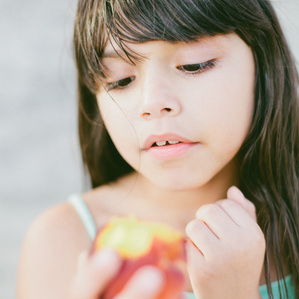 Girl stares at peach before taking a bite