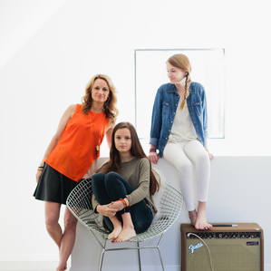 Mother stands next to teenage daughters in home
