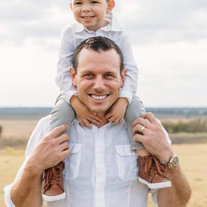 Craig dahl and son on his shoulders stand together in pasture