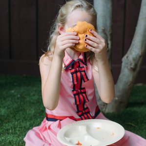 Girl sitting on ground covers face with burger