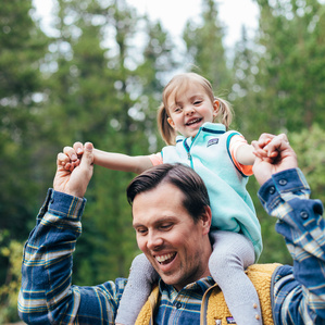 Father holds daughter on shoulders while walking through park