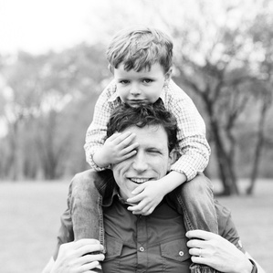 Son sits on Dad's shoulders with hand over his eye