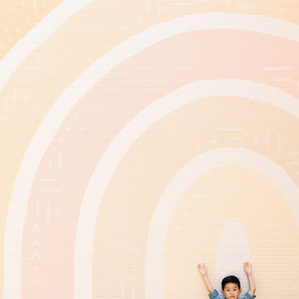 Little boy with hands up next to rainbow mural wall