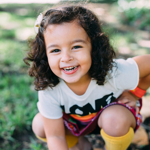 Girl leans down in front yard smiling at camera