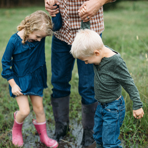 Son and daughter hold hands of Father while jumping in mud puddle