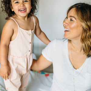 Mom smiles at daughter laughing on bed