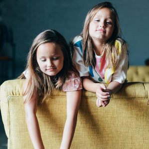 Twin sisters hang over back of yellow couch