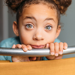 Little girl with hair buns sits behind chair