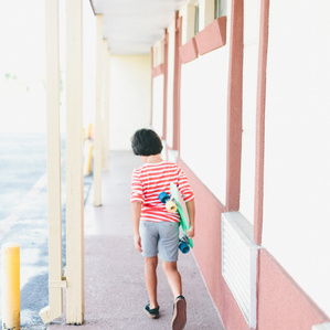 Boy walks along breezeway with skateboard