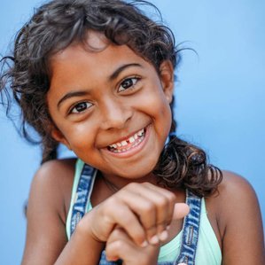 Happy girl with curls stands by blue wall smiles