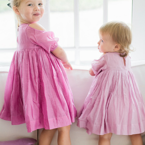 Sisters in dresses lean over couch next to window