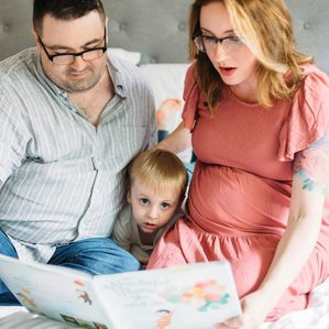 Dad and pregnant Mother read to their child on bed