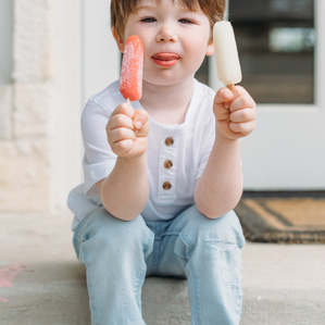 Boy sits with two popsicles on back porch