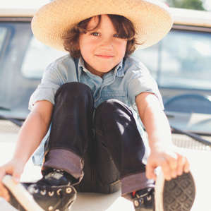 Little boy sits on top of car hood with a hat