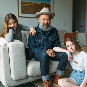 Father sits with two teenage daughters in living room