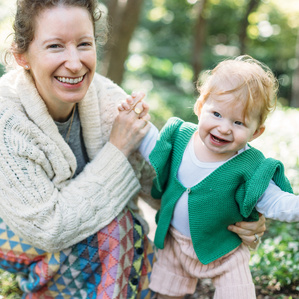 Mother bends down next to daughter and smiles together in a park