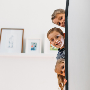 3 siblings peek around stairs in home