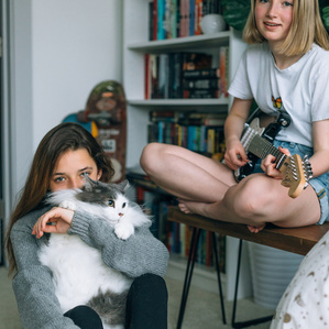 Two teenage sisters in bedroom with cat and guitar