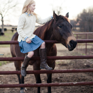 Young girl sits on fence next to her horse