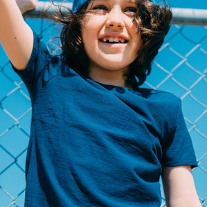 Boy stands by fence smiling in the sun