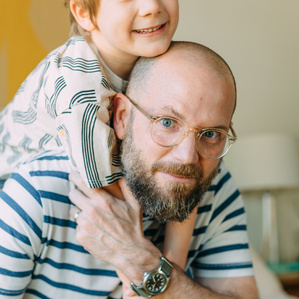 Father embraces son on his back in bedroom