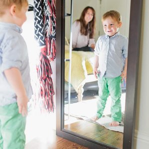 Boy admires himself in mirror while Mom smiles behind him