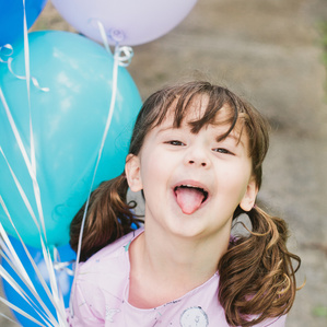 Little girl holding balloons sticks out tongue