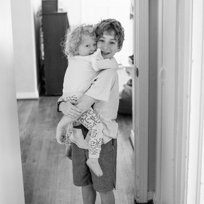 Big brother holds little sister in hallway in black and white