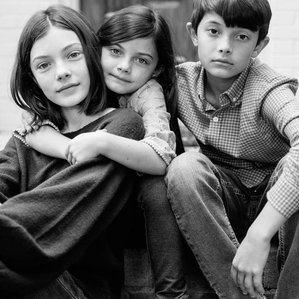 Three kids sit together on front steps of home