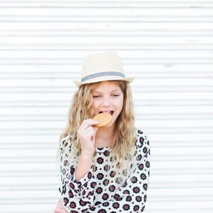 Girl with fedora hat and cookie stands by metal wall