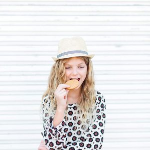 Girl with fedora hat and cookie stands by metal wall