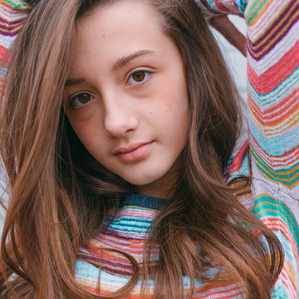 Teen girl with colorful striped shirt and long hair holds arms above head