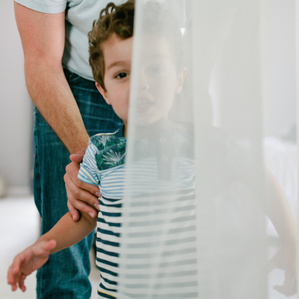 Boy peaks through curtain while Dad stands behind him