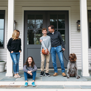 Family of four with teenagers stand outside on porch with dog