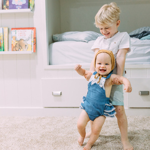 Brother holds little sister who is learning to walk
