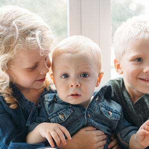 Three siblings with blonde hair sit together in window