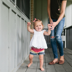 Baby girl takes first steps near Mom on porch