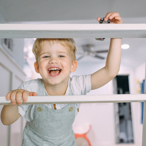 Little boy in overalls laughs at camera on ladder