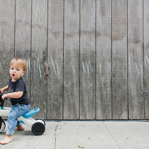 Little boy sits on tricycle next to wood wall