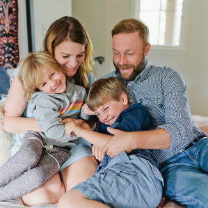 Family of 4 cuddles and tickles each other on bed